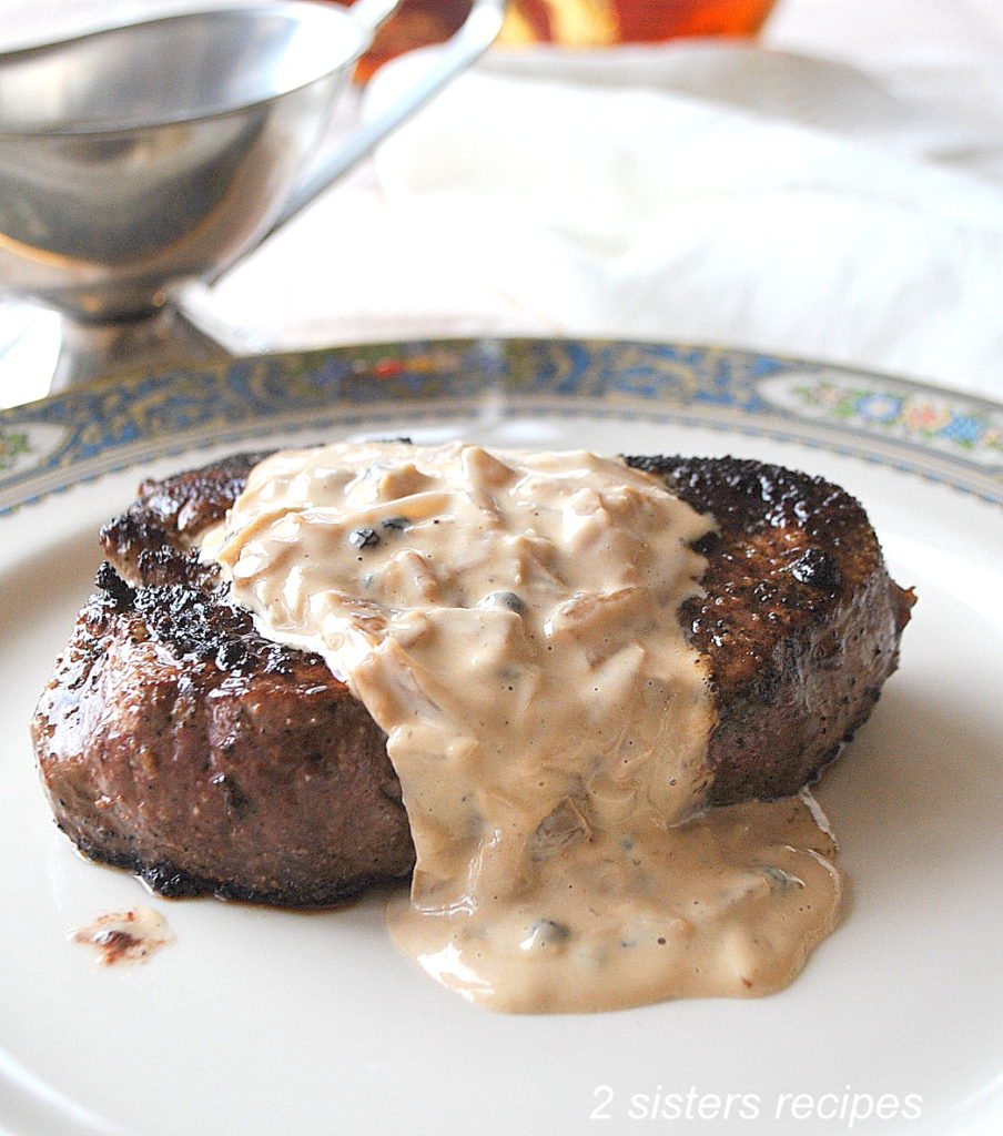 On a white plate is served a grilled steak with a creamy peppercorn sauce on top.