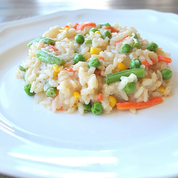 A white dinner plate with a serving of vegetable loaded risotto.