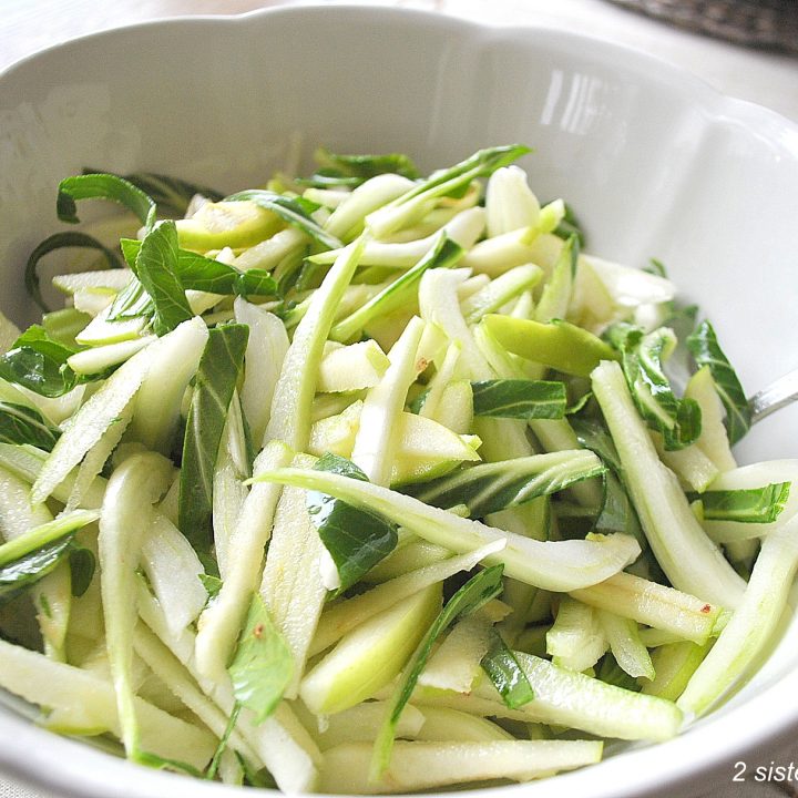 A white salad bowl with sliced apples, and sliced Bok Choy.