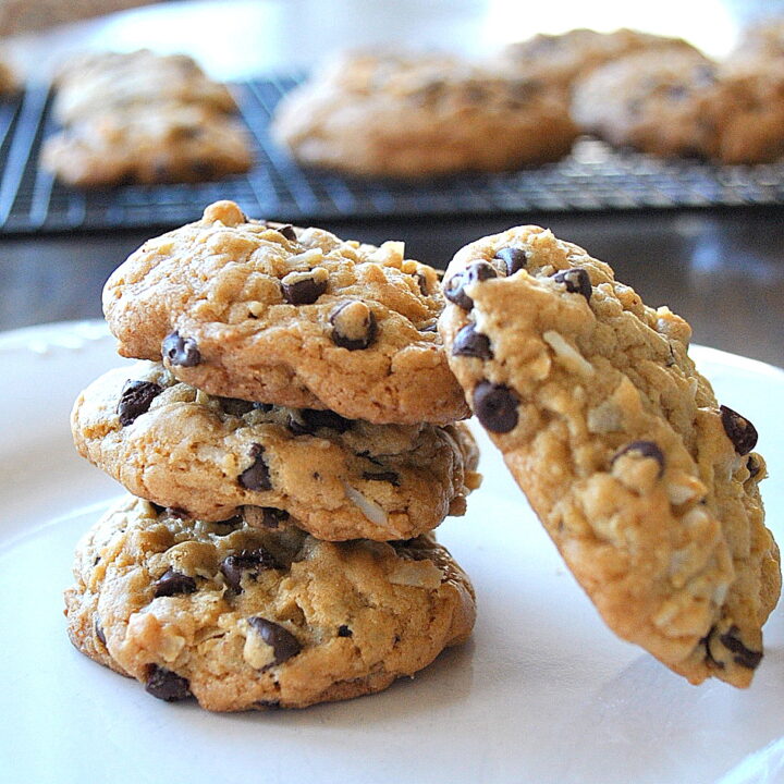 A pile of 3 Chocolate Chip Coconut Cookies on top of one another with one on its side on a white plate.