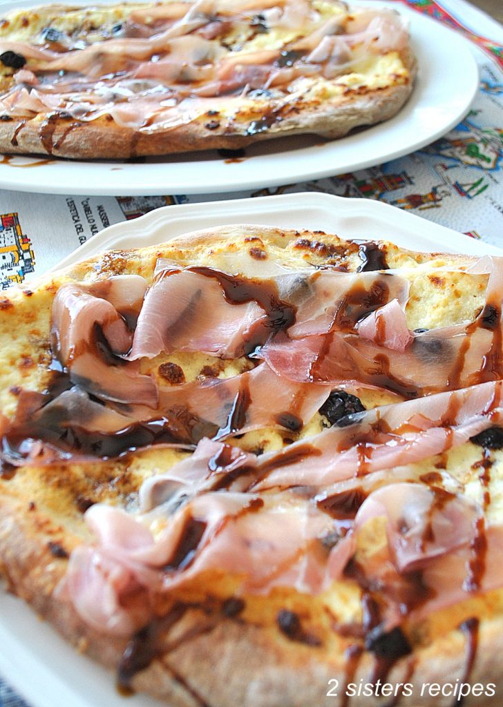 A round pizza with melted cheeses, sliced prosciutto and cherries on top.
