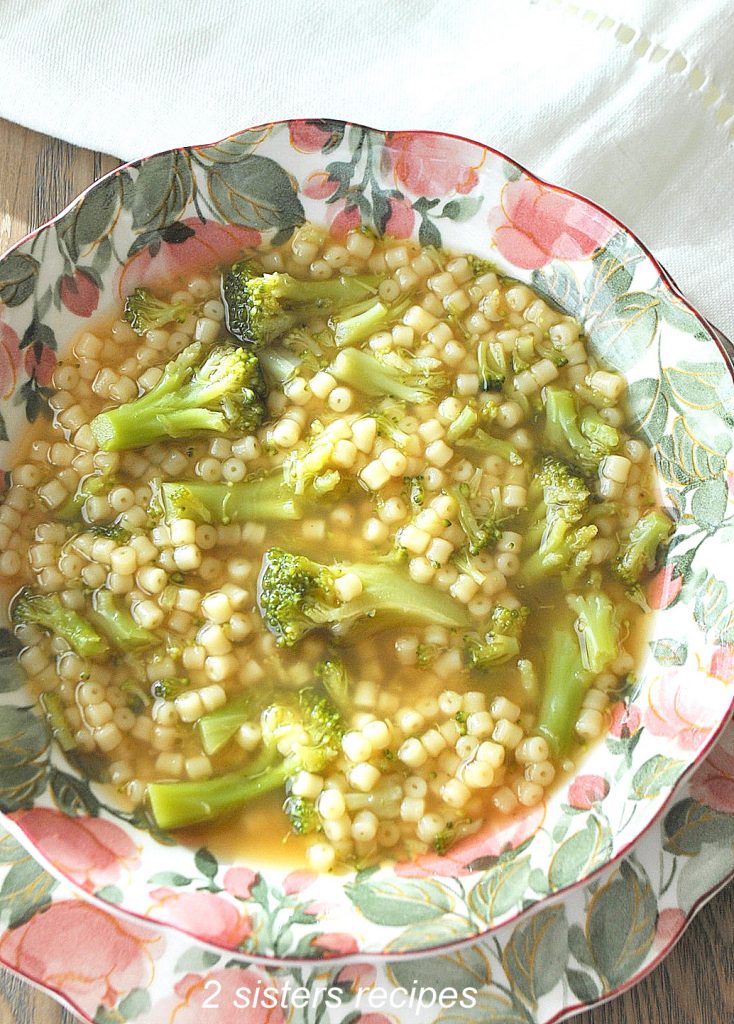 A pink and green bowl filled with a broccoli and little pasta soup.