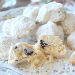 A plate of white powdered ball-shaped cookies with one cookies sliced in half.