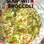 A pink and green bowl filled with little pasta and broccoli florets in a soup.