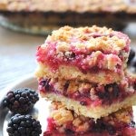Three blackberry crumble bars are piled on a plate.