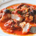 A forkful of Cod Livornese served on a white dinner plate.