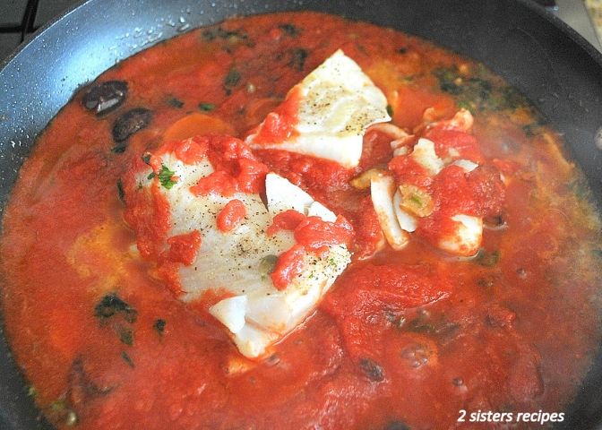 A skillet with tomatoes, olive and cod fish simmering,. by 2sistersrecipes.com
