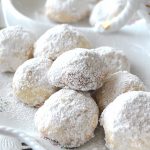 A ceramic white dish filled with bite-sized cookies covered with white powdered sugar.