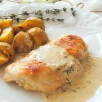 Grilled chicken breast is served on a white dinner plate with Dijon Sauce over it and roasted potatoes on the side.
