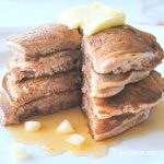 A pile of pancakes with butter and maple syrup on top served on a white plate.