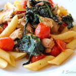 A white dinner plate with penne pasta, cherry tomatoes and kale mixed into the pasta.