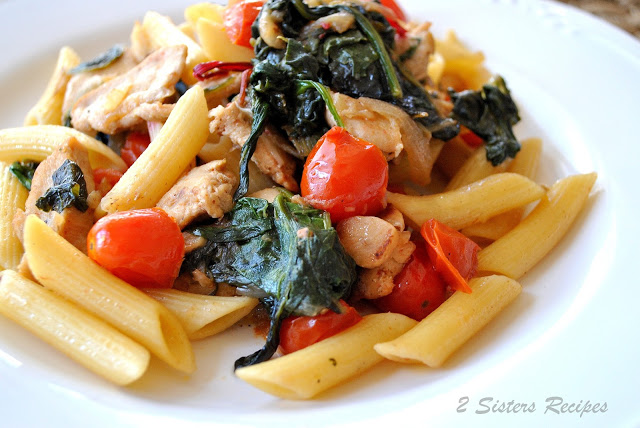 A white dinner plate with penne pasta, cherry tomatoes and kale mixed into the pasta. 