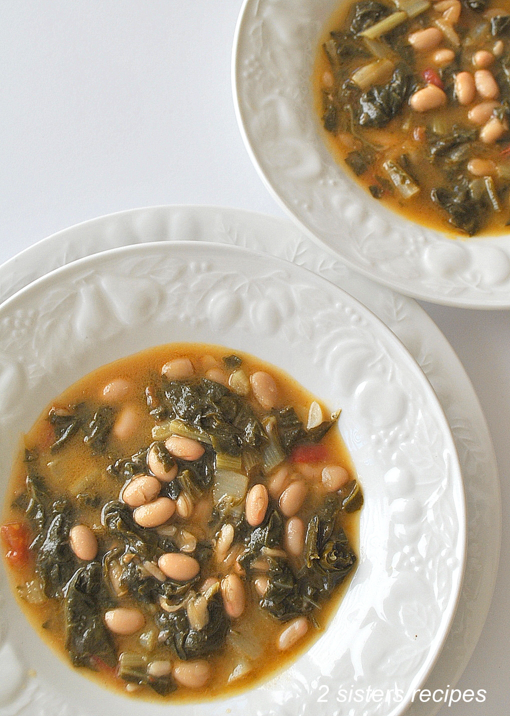 Two white soup bowls filled with a soup made with white beans and Swiss Chard.