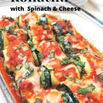 A glass baking dish filled with zucchini roll ups stuffed with spinach and cheese and topped with tomato sauce.