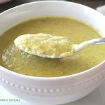 A white bowl of broccoli and leek soup with a spoonful over the bowl.