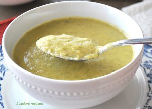 A white bowl of broccoli and leek soup with a spoonful over the bowl.