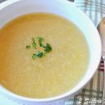 A white soup bowl filled with a pureed celery soup with some chopped parsley on top.