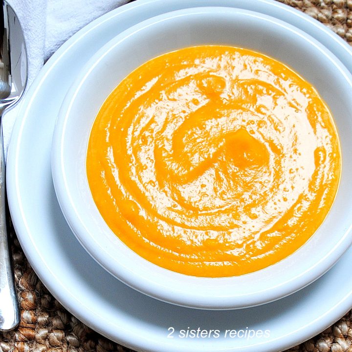 A white bowl over a dinner plate filled with a thick pureed butternut squash potato soup.