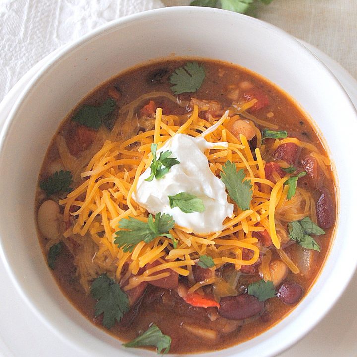 A white bowl of beans, and vegetables with shredded cheese and some sour cream on top.