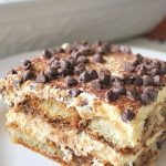 A square piece of Tiramisu cake on a white plate.
