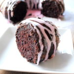 A slice of chocolate cake with pink icing drizzled on top served on a white plate.