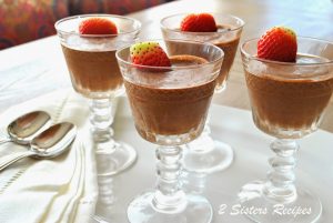 Four cordial glasses filled with chocolate mousse and topped with a strawberry.