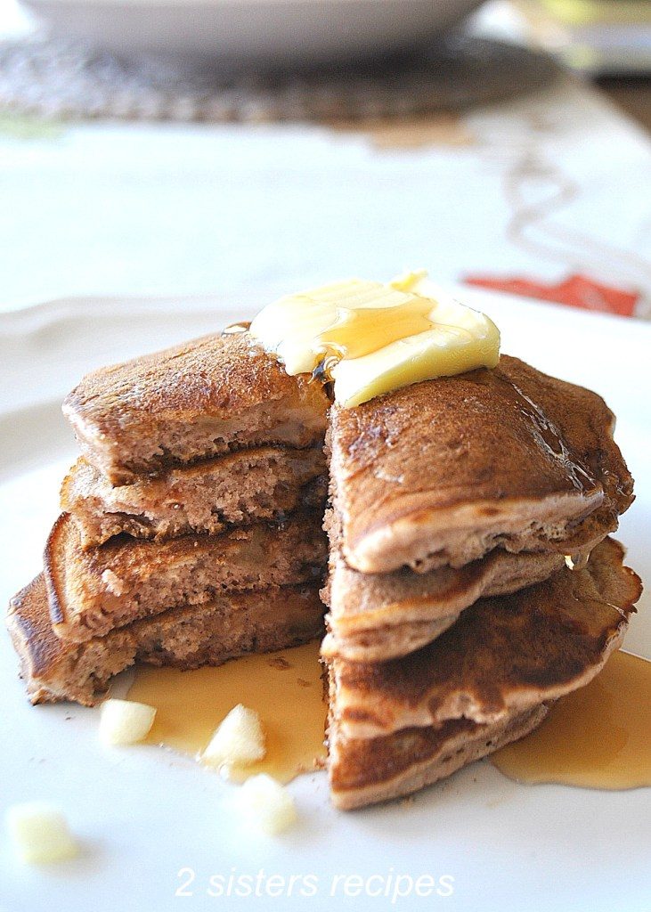 A white plate with pancakes filed up high with butter and maple syrup on top.