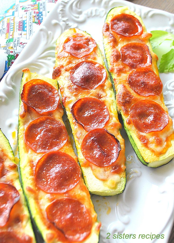 There are 4 Zucchini Pepperoni Pizza Boats served on a white platter.