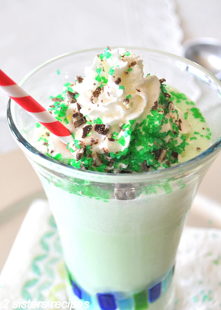 Frozen Grasshopper drink served with whipped cream on top and a red and white strip straw in a tall glass.