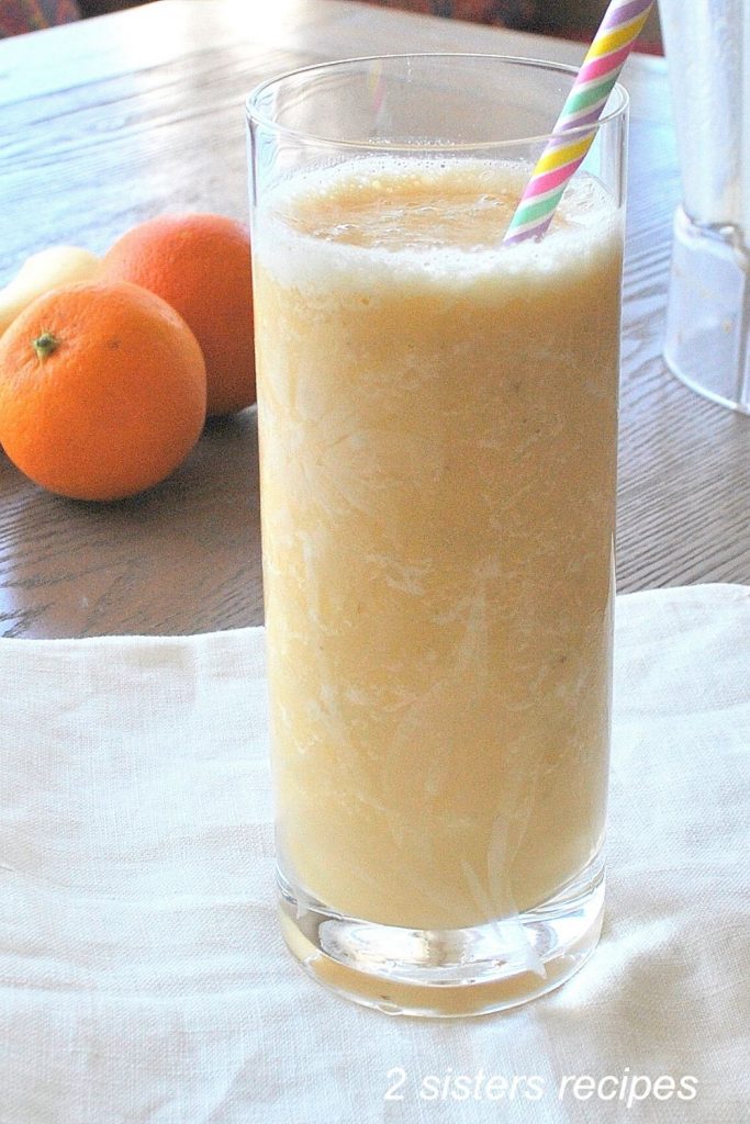 A tall glass of Orange smoothie with a staw and navel oranges beside the glass.