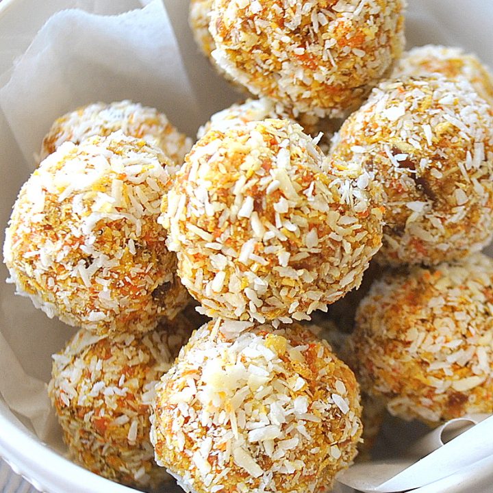 A white bowl filled with carrot cake bites coated in shredded coconut.