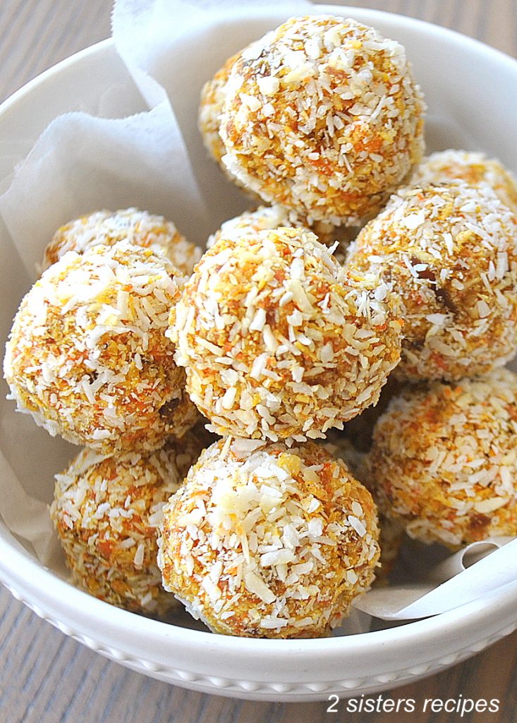 A white bowl filled with carrot cake bites coated in shredded coconut.