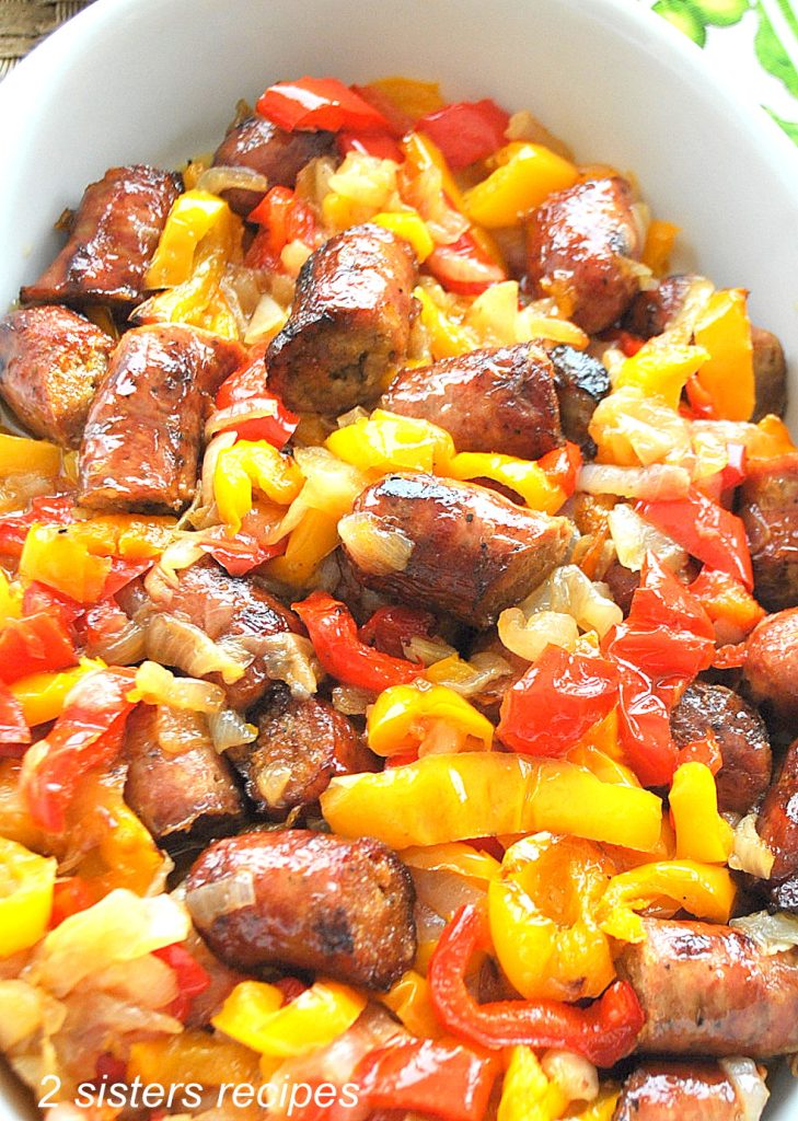 A white oval platter filled with a mixture of baked sausage and red and yellow peppers.