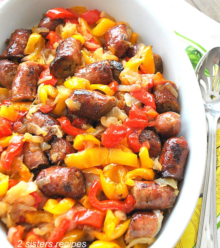 A white oval casserole dish filled with  baked colorful peppers and chopped sausages. 