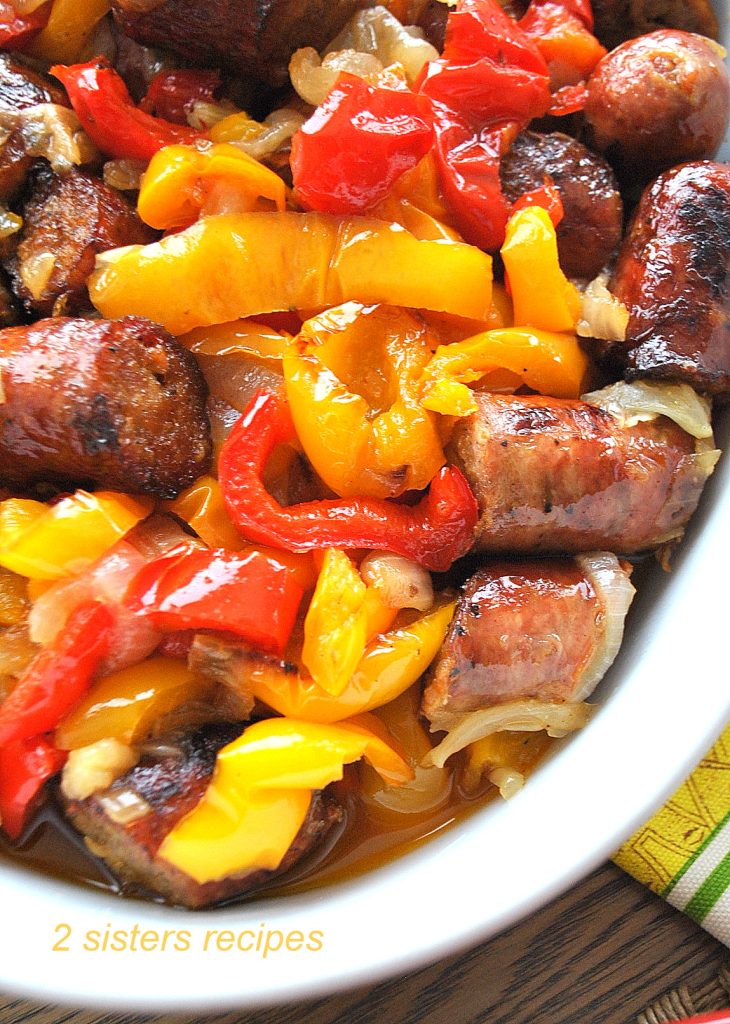 An array of colorful peppers and pieces of sausages in a white baking dish.  by 2sistersrecipes.com