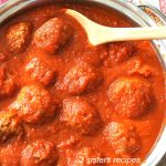 A large skillet filled with tomatoes sauce and meatballs and a wooden spoon.