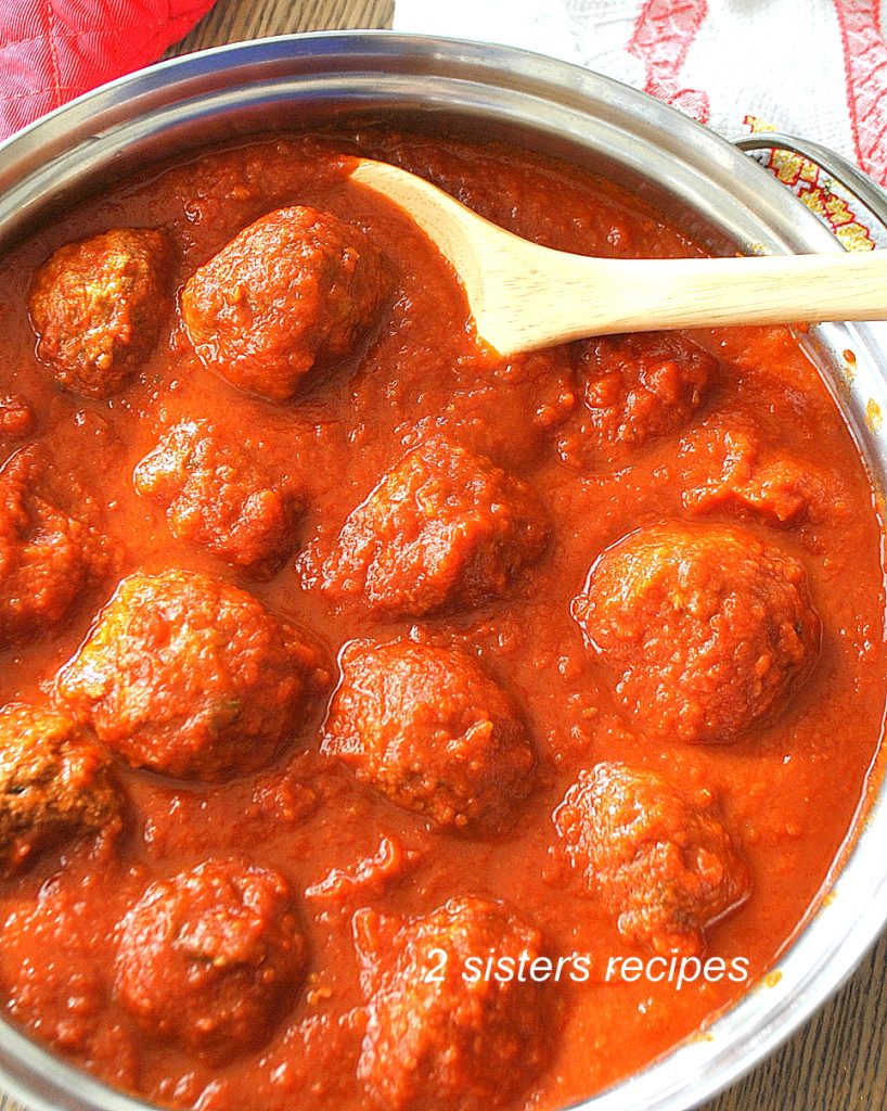 A large skillet filled with tomatoes sauce and meatballs and a wooden spoon.