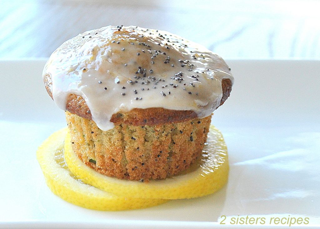 Lemon Zucchini Poppy Seed Muffin is sitting on a lemon slice on a white plate.
