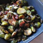 A square dark colored bowl filled with roasted Brussels sprouts with bacon.