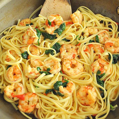 A skillet filled with linguine pasta, shrimp, red peppers, and spinach.