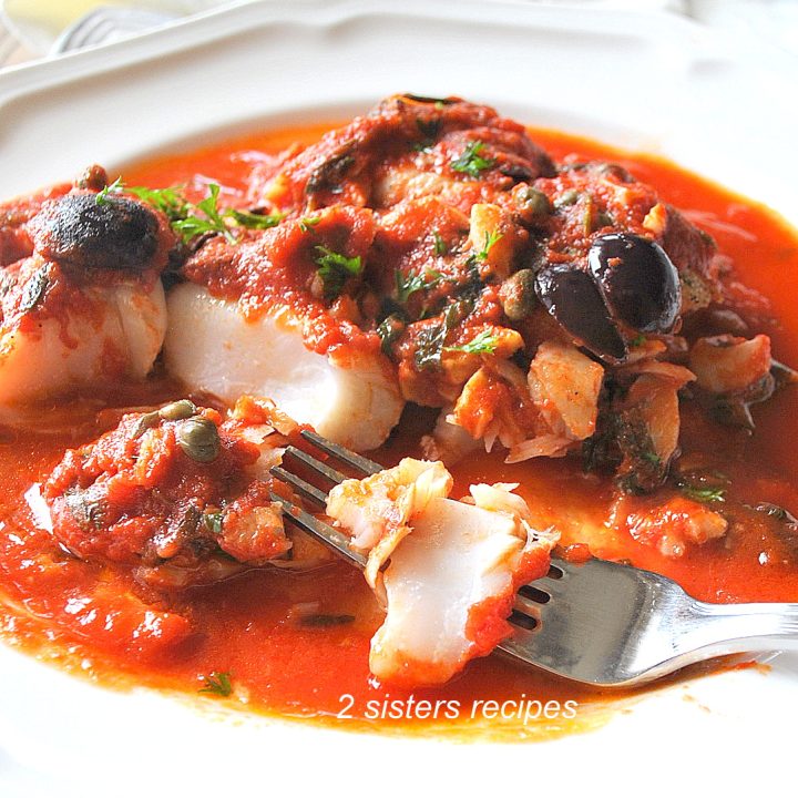 A white serving plate with a cooked codfish smothered in a tomato sauce.