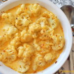 A round white baking dish loaded with cauliflower covered with melted cheese sauce.