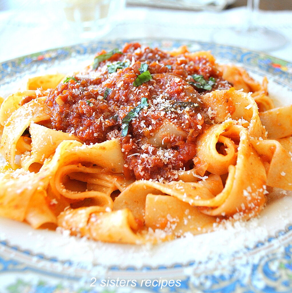A blue and white dinner plate filled with pappardelle pasta and topped vegetable Bolognese and topped with grated cheese.
