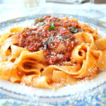 A blue and white dinner plate filled with pappardelle pasta and topped vegetable Bolognese and topped with grated cheese.