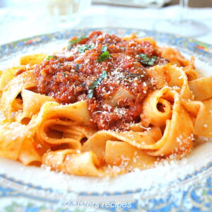 A blue and white dinner plate filled with pappardelle pasta and topped vegetable Bolognese and cheese.