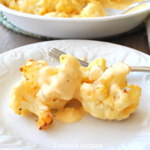 Cauliflower loaded with melted cheese on top on a white serving plate.