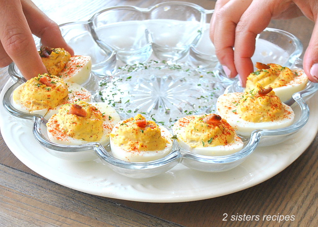 two hands are grabbing a deviled egg from the plate.