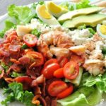 A bed of lettuce served on a plate, topped with sliced tomatoes, eggs, avocado, and chunks of steamed lobster meat.