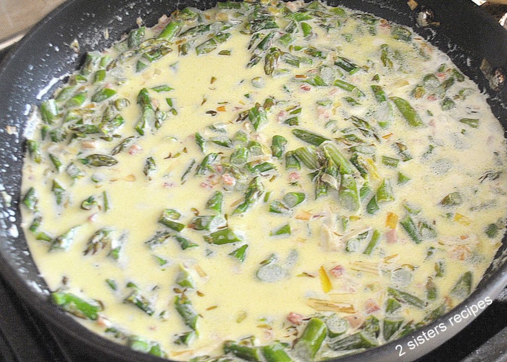 A skillet with chopped asparagus simmered in a white cream sauce. by 2sistersrecipes.com 