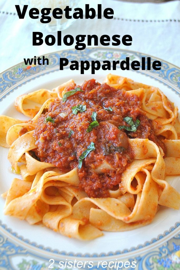 A white and blue dinner plate filled with pappardelle noodles with a thick, chunky vegetable tomato sauce on top.